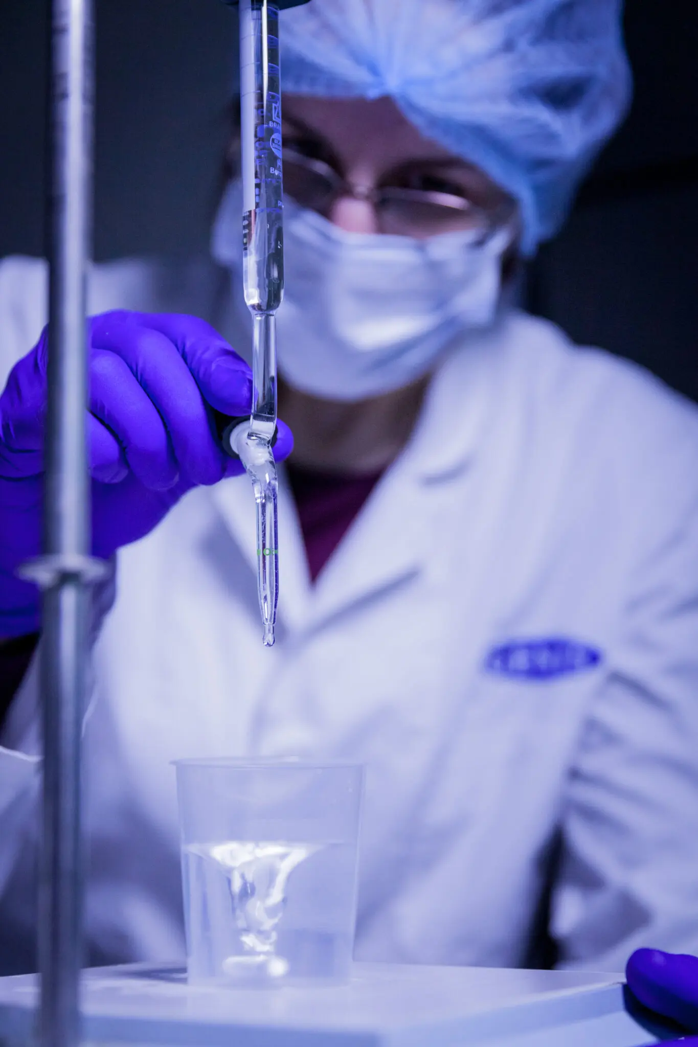 Scientist in a laboratory carefully dispensing liquid from a glass pipette into a container, illustrating biomaterial research at Genis.